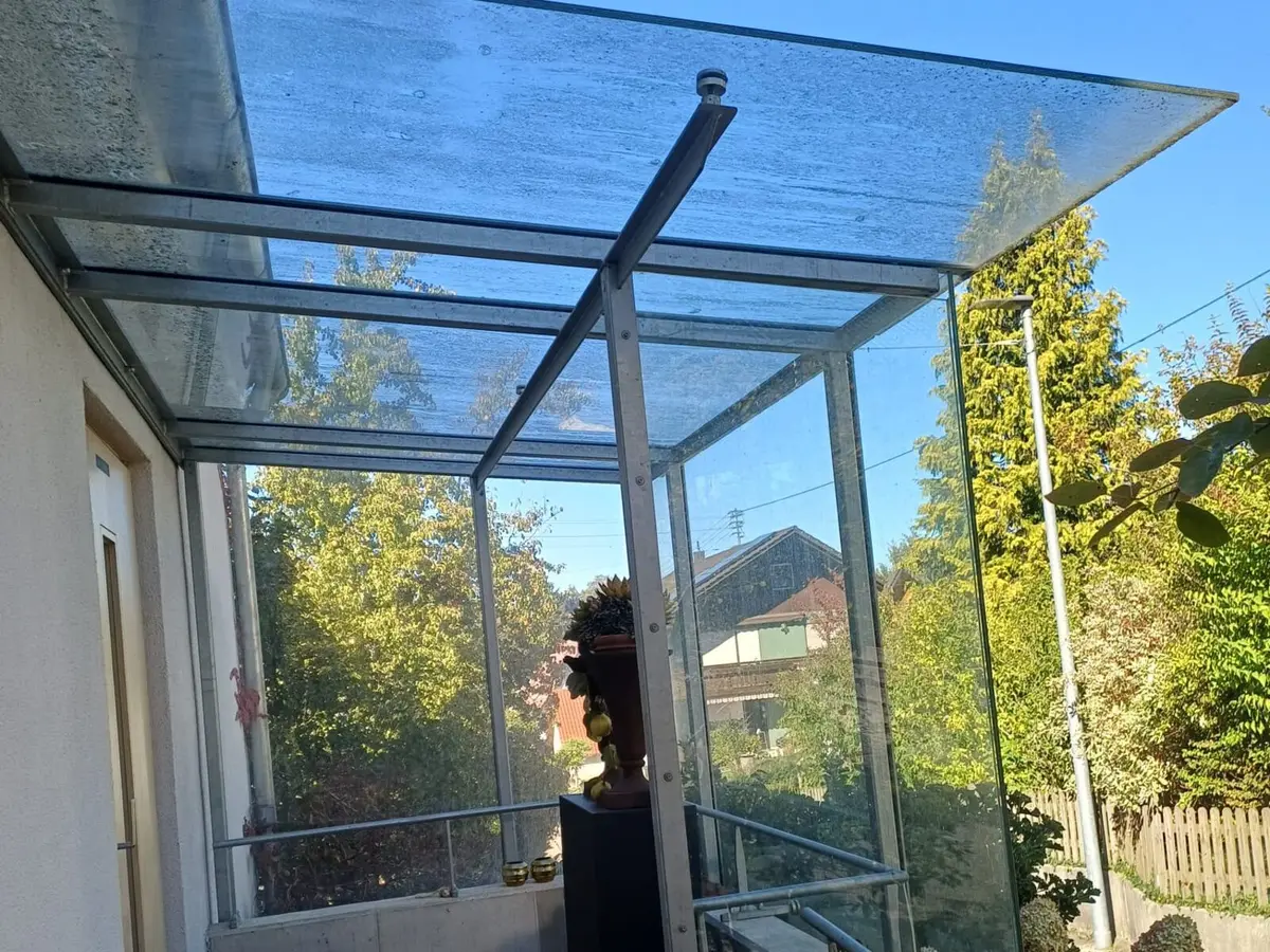Gläsernes Vordach über einem Hauseingang mit Kalkflecken und Schmutz auf dem Glas vor der Reinigung
